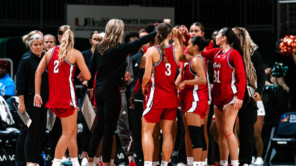 woman basketball coach stands in crowd of college aged women basketball players in red jerseys