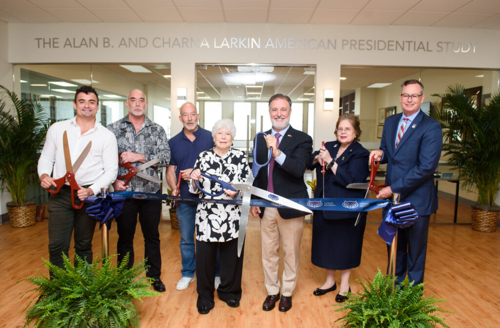 adults with large scissors stand in front of blue ribbon acting like they are about to cut ribbon