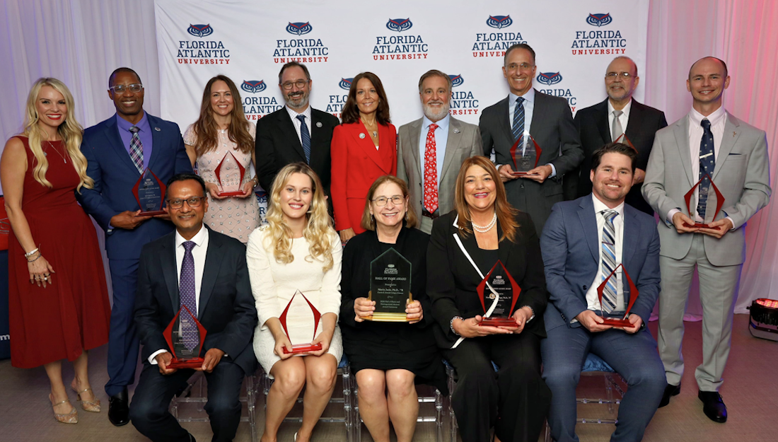 group of adults with awards sit and stand for a picture in front of a backdrop