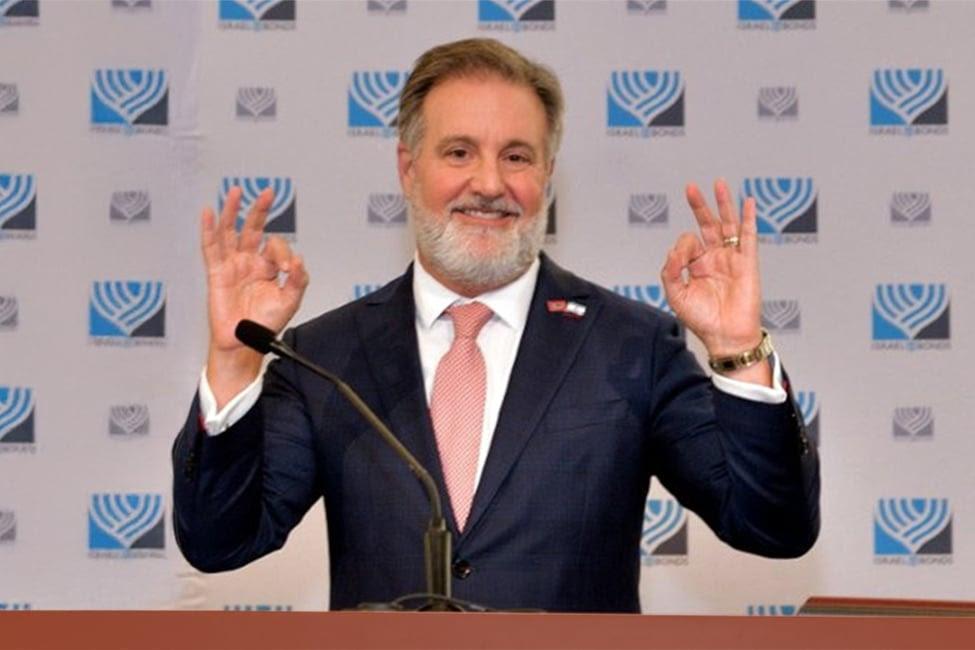 mean with beard stands at podium holding his pointers to his thumbs