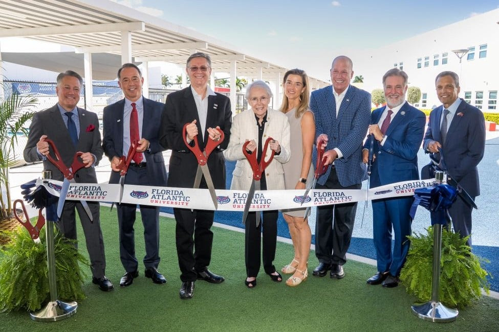 group of adults stand in front of a ribbon with large scissors ready to cut the ribbon