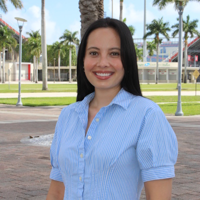 headshot of woman in blue dress with baseball stadium behind her