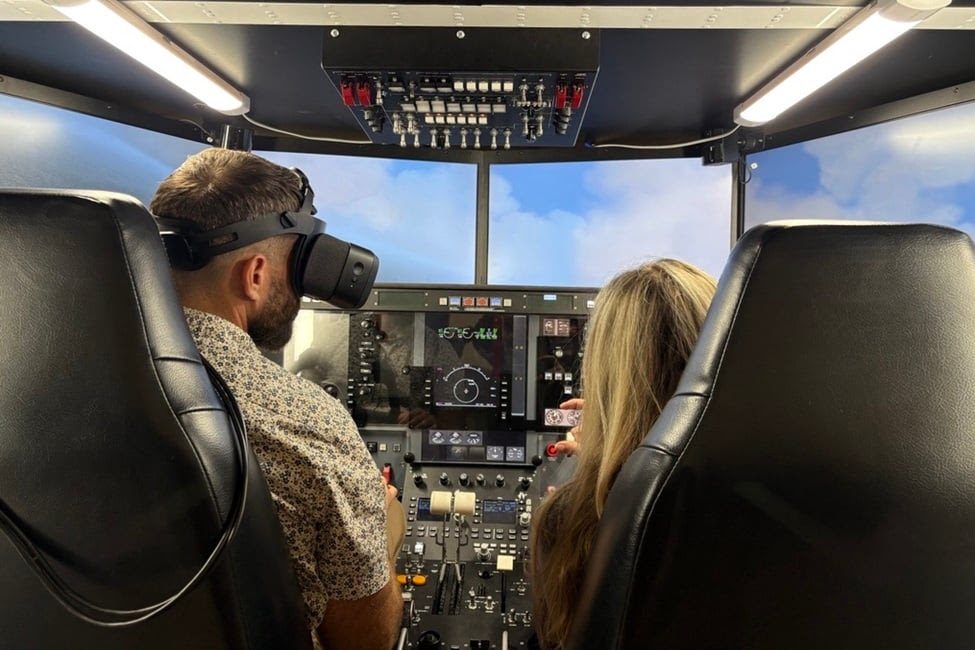 man with VR headset sits next to woman in plane simulator