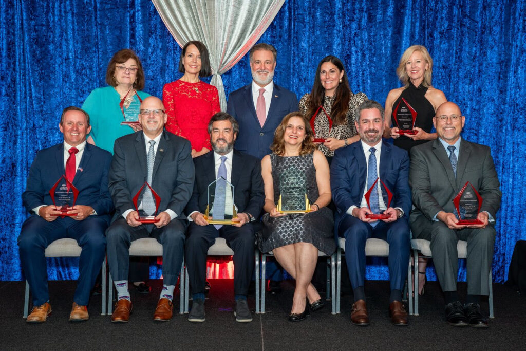 two rows of adults holding glass awards with the back row of people standing and the front row sitting in chairs