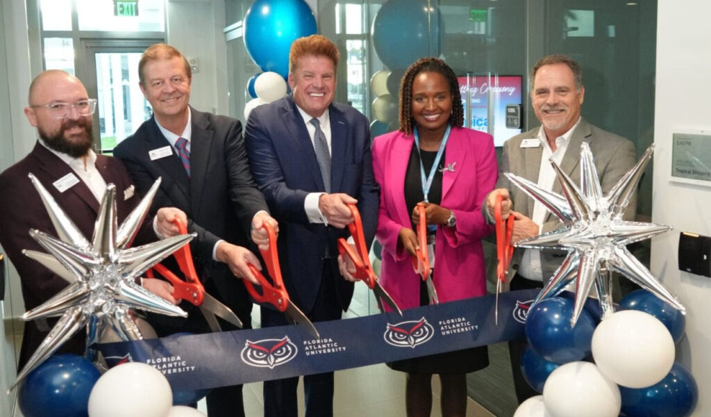 group of adults stand with over-sized scissors pretend to cute a ribbon
