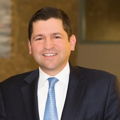 headshot of man in suit with light blue tie and blurred background