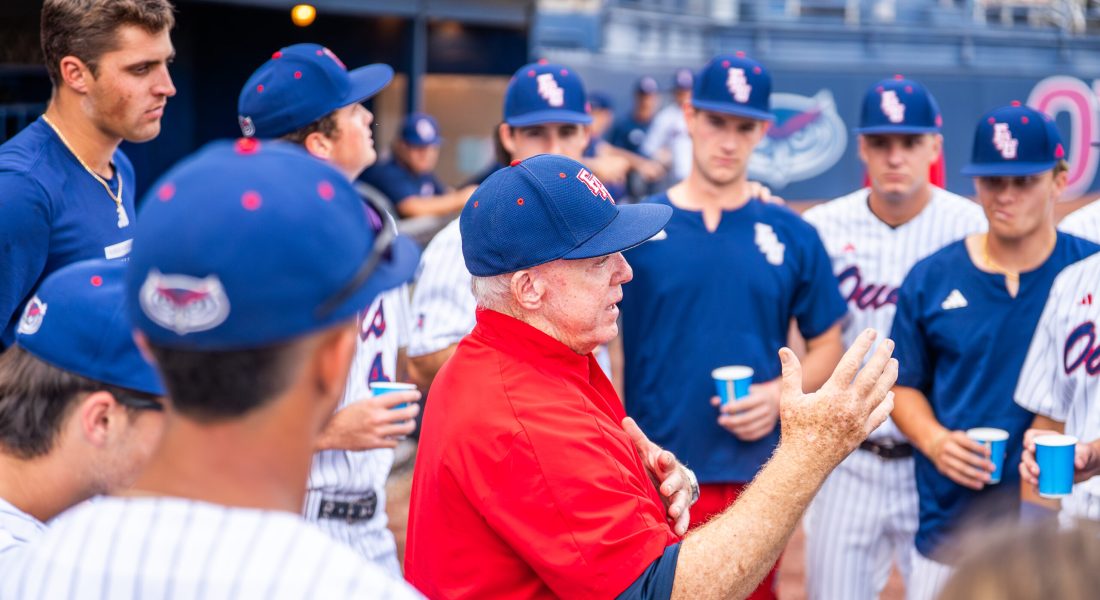 baseball coach stands in center of a group of college ages baseball players
