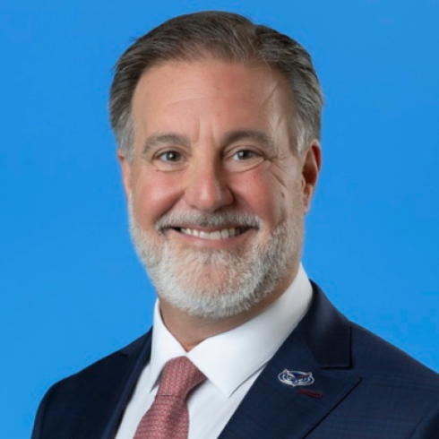 headshot of man in suit and tie with a bright blue background